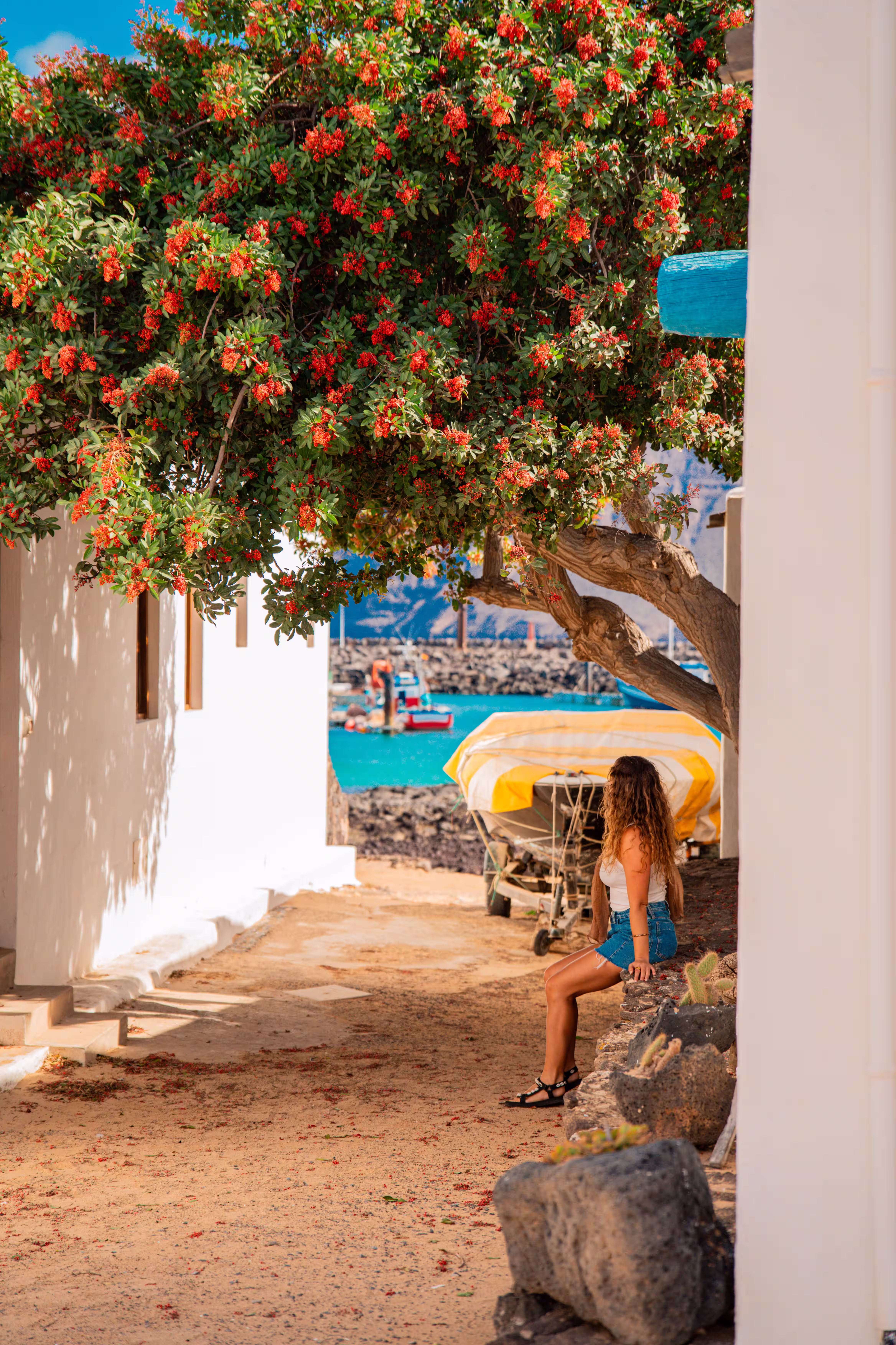 Mujer sentada bajo un árbol en una calle de arena de La Graciosa